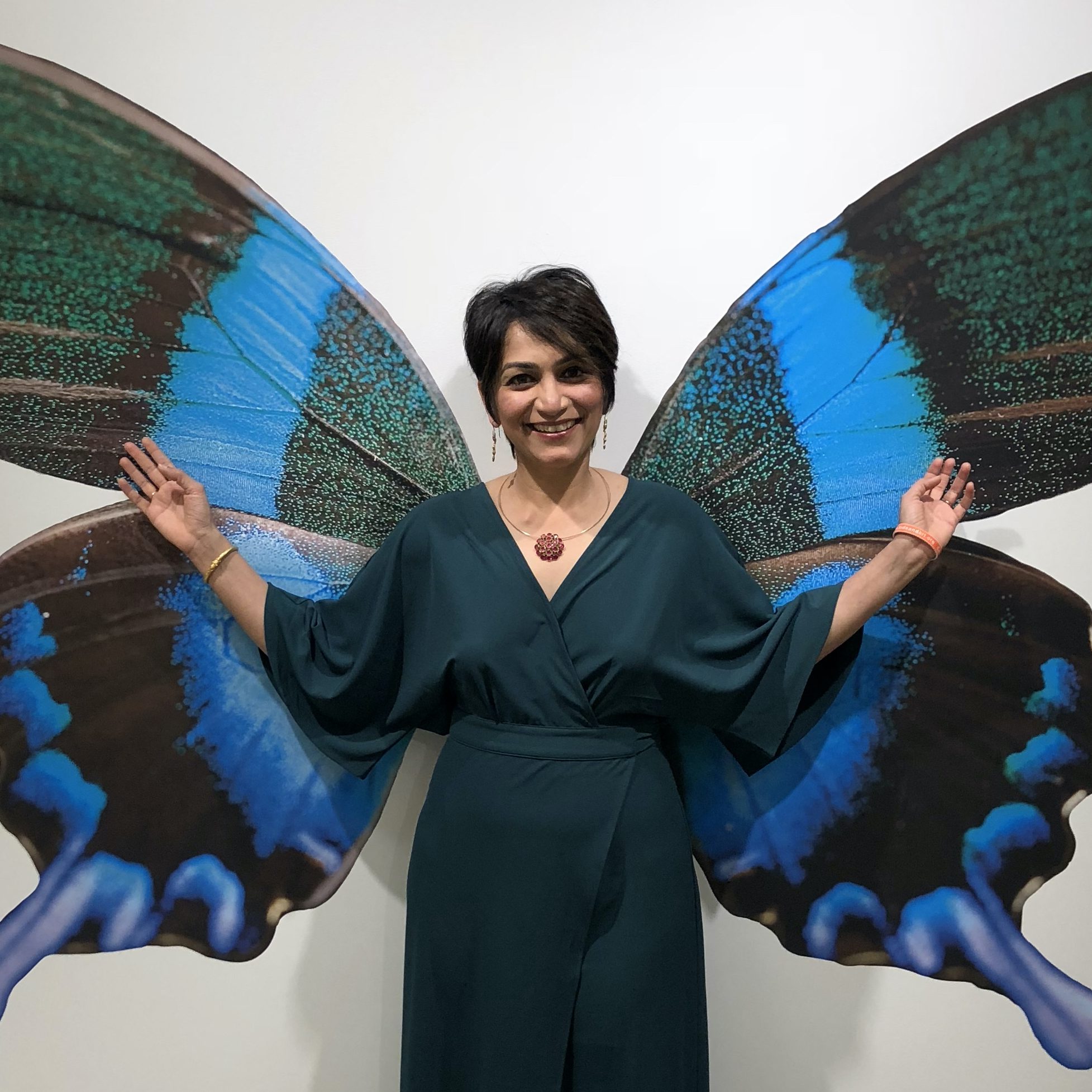 image: purvi shah wearing blue, standing in front of wall with butterfly mural